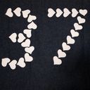 Twenty six little white paper hearts arranged into the digits thirty seven laid on dark denim.