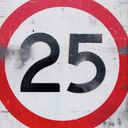 A battered reflective speed limit sign. The speed limit is twenty five.