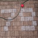 A garden hose snakes across chalk shaded outdoor pavers, as pixels the pavers spell seventy nine in big digits. A bright red plastic ball rests against the hose.