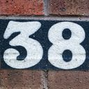 The digits of thirty eight are rendered in white on a black textured tape stuck to a brick wall.